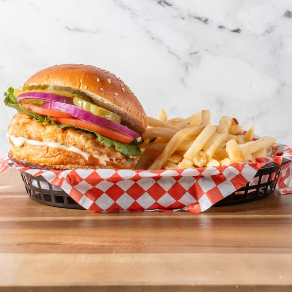 Chick-N-Guys fried chicken sandwich with lettuce, tomato, onion, pickles, and fries in a basket.