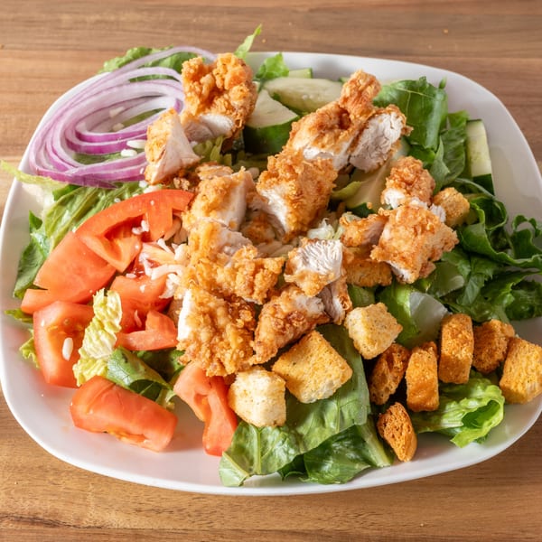 Crispy fried chicken pieces, red onions, tomatoes, and croutons on a fresh green salad.