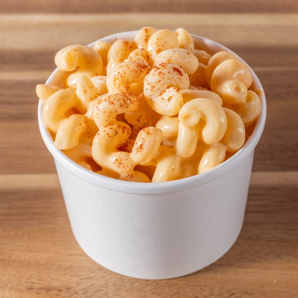 A white cup filled with creamy macaroni and cheese, sprinkled with paprika, on a wooden surface.