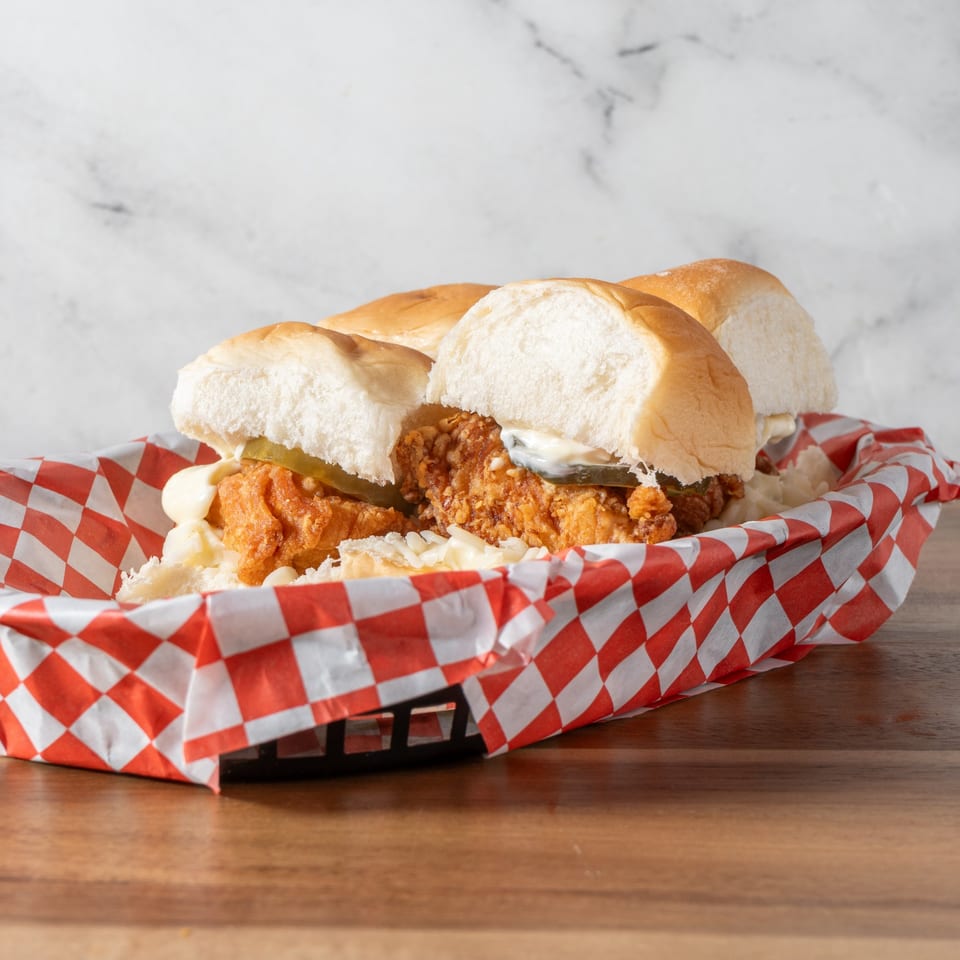 Three Chick-N-Guys fried chicken sliders with pickles and mayo in a red and white checkered basket.