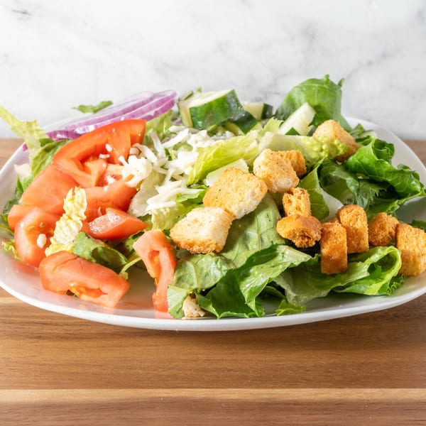 Fresh garden salad with lettuce, tomatoes, red onions, cucumbers, shredded cheese, and croutons.