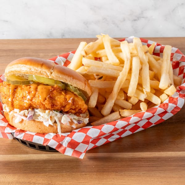 A Chick-N-Guys fried chicken sandwich with pickles, sauce, and coleslaw, served with fries.