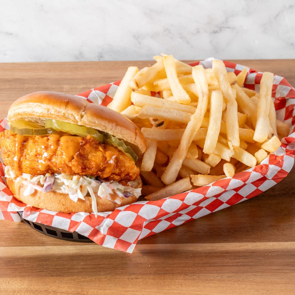 A Chick-N-Guys fried chicken sandwich with pickles, sauce, and coleslaw, served with fries.