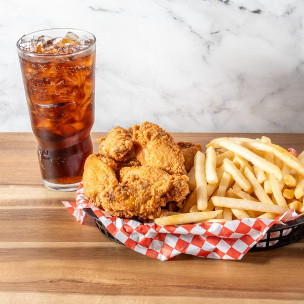 Chick-N-Guys fried chicken and french fries in a basket with a soda on a wooden table.