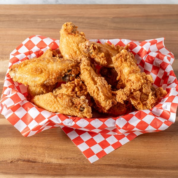 Crispy fried chicken pieces in a red and white checkered paper-lined basket on a wooden table.