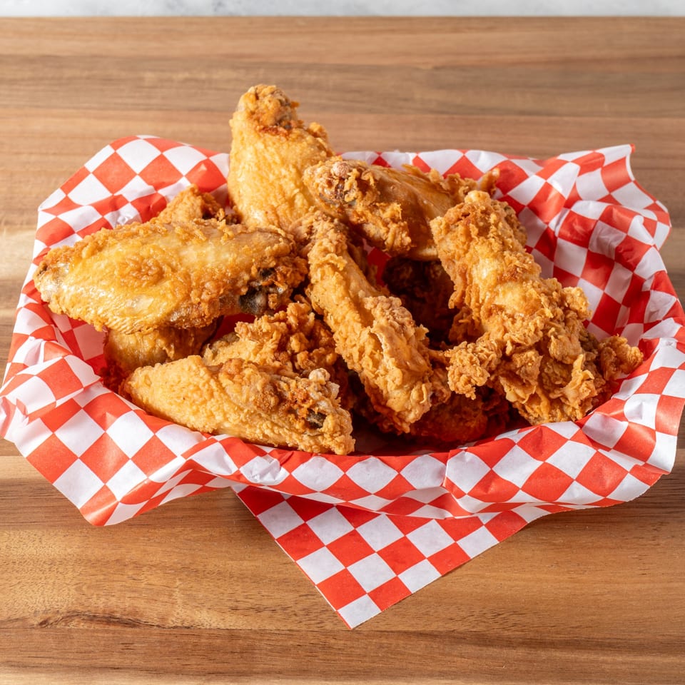 Crispy fried chicken pieces in a red and white checkered paper-lined basket on a wooden table.